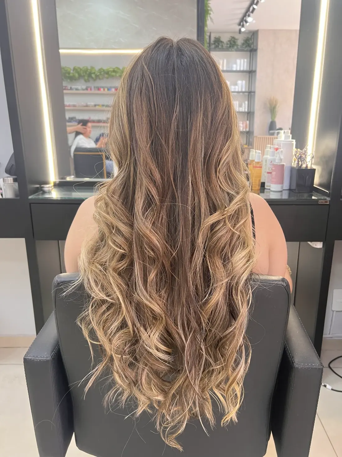Cabelo loiro com mechas, cliente de costas em cadeira de salão